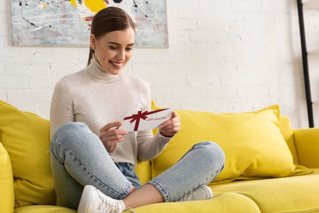 Smiling young woman with gift voucher on sofa in living room