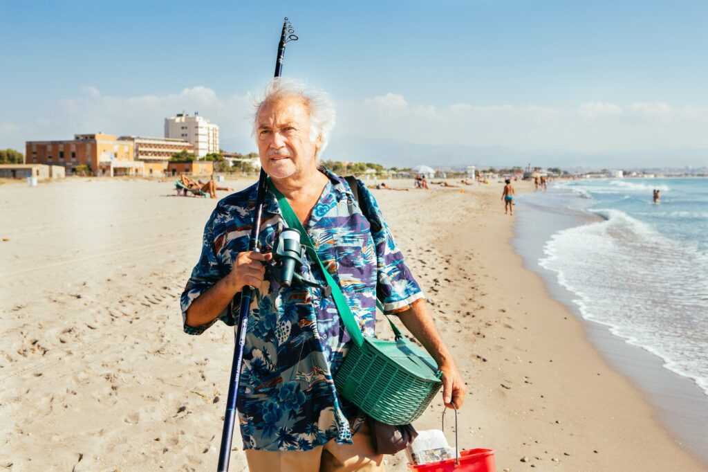 An elderly man fishing on the beach in a sunny day.